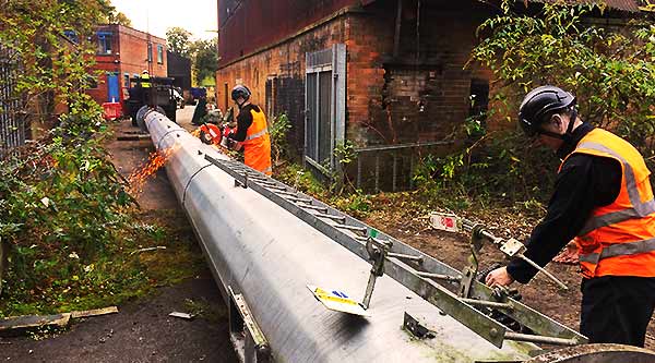 distance view of a massive commercial industrial hollow metal tower laid down on its side with two howarths scrap men disposal experts over seeing the entire removal process