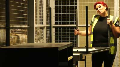 distance view of a high visibility uniformed female howarth employee lifting an office desk and smiling at the camera