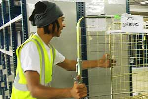 close up photo of a young man pushing a basket cage on wheels that is loaded with shelving and racking