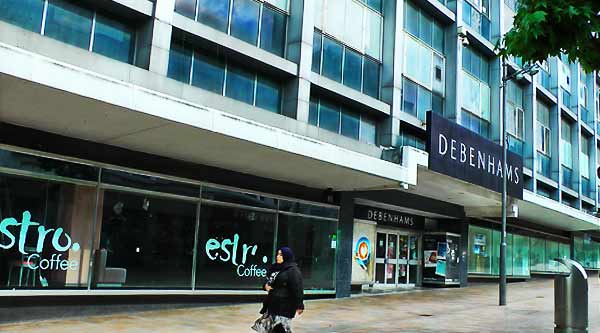 distance ground floor external photo of retail giant debenhams in sheffields town center showing all its huge mass including many large windows reflecting the dim sun light and the grand side moor entrance doors